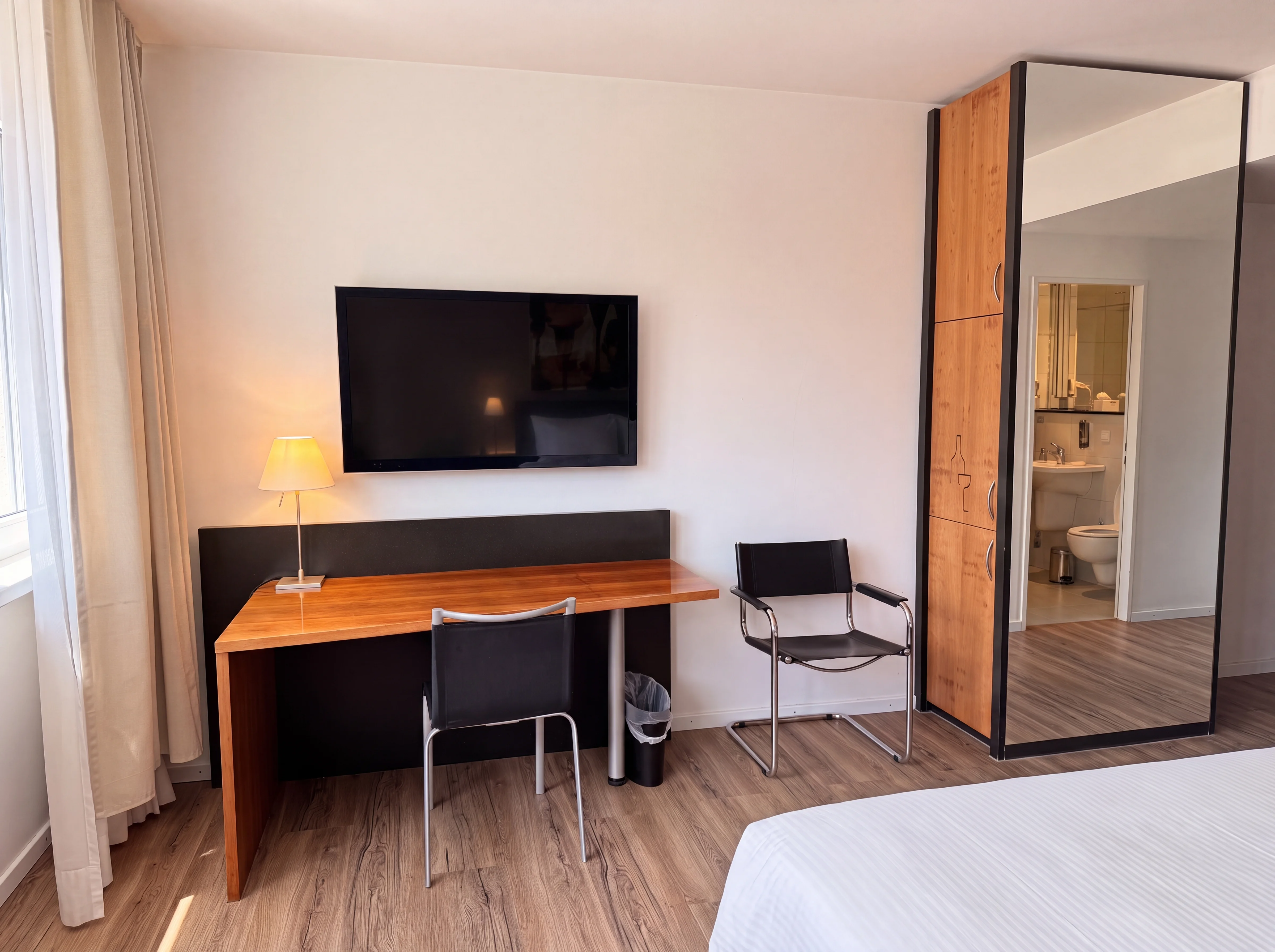 Arbeitsplatz mit Schreibtisch, Flachbild-TV und Spiegelschrank im Businesszimmer