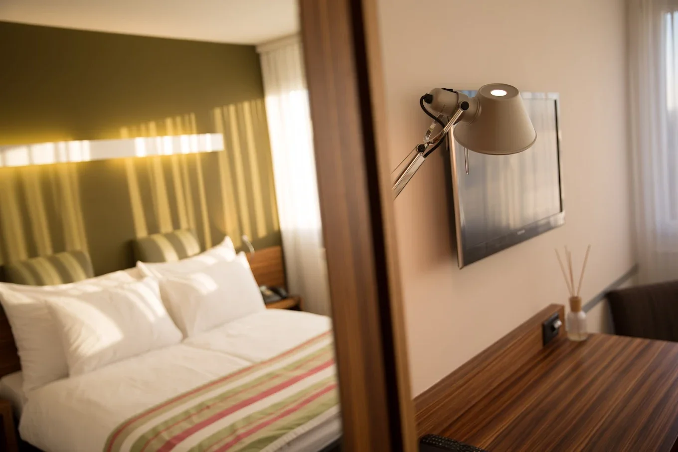 Blick ins Zimmer: Bett mit gestreifter Tagesdecke, Leselampe und Schreibtisch, Hotel Belair Wallisellen